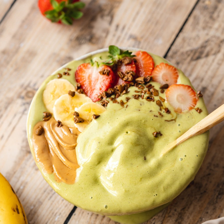 Green smoothie bowl with fruit on a wooden table