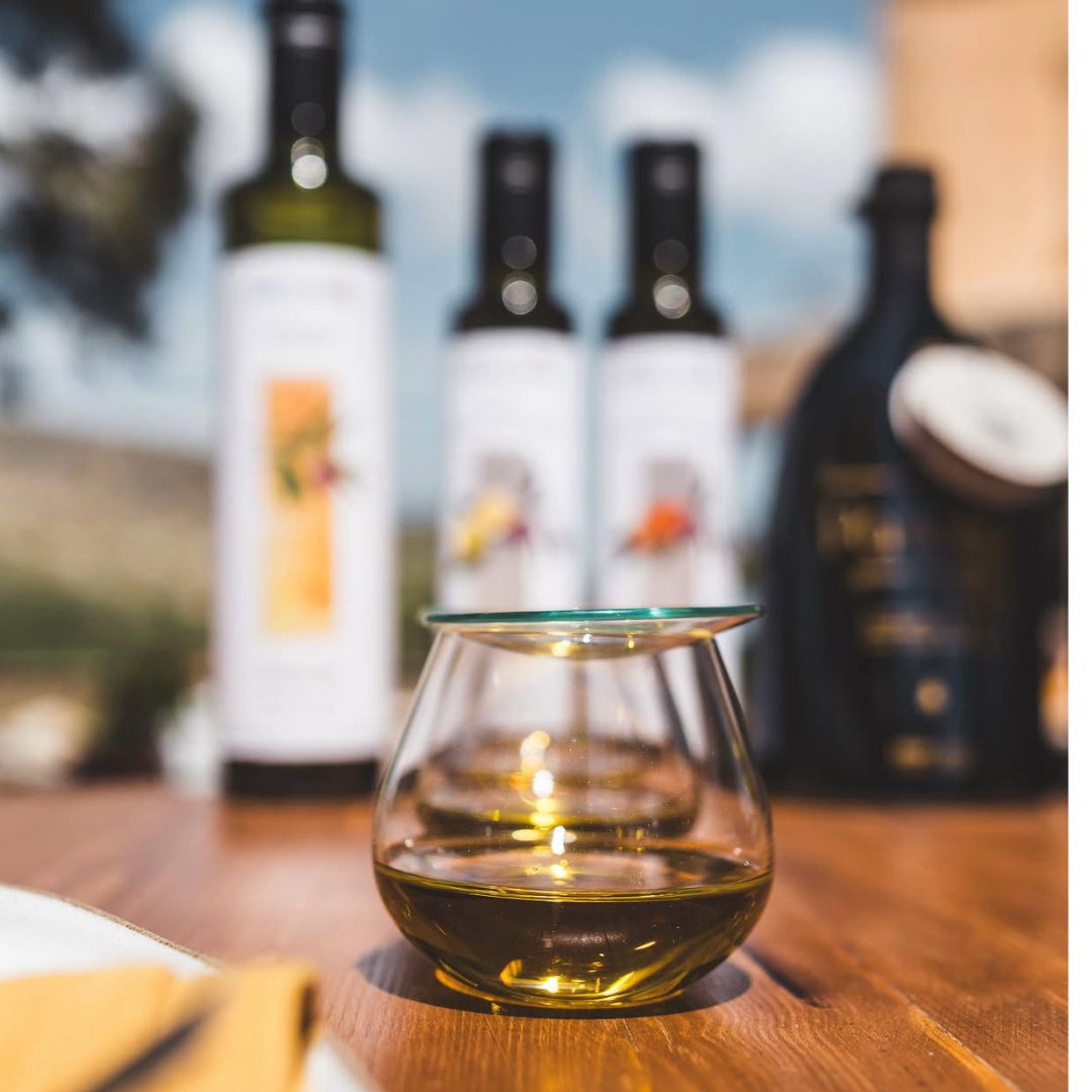 Olive oil tasting glass with bottles in the background